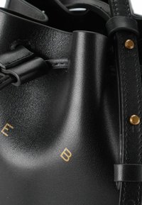 Bolso de cuero negro con acabado texturizado, cierre de cordón y acentos en dorado. Presenta un logotipo visible en dorado en el exterior.