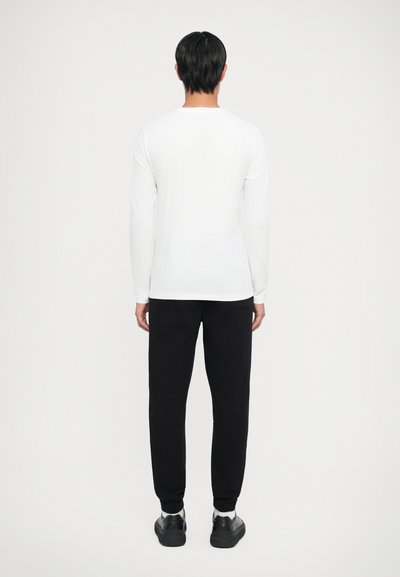 Cămașă albă cu mânecă lungă combinată cu pantaloni de trening negri. Design simplu și ajustat, textură netedă și accente minimaliste.