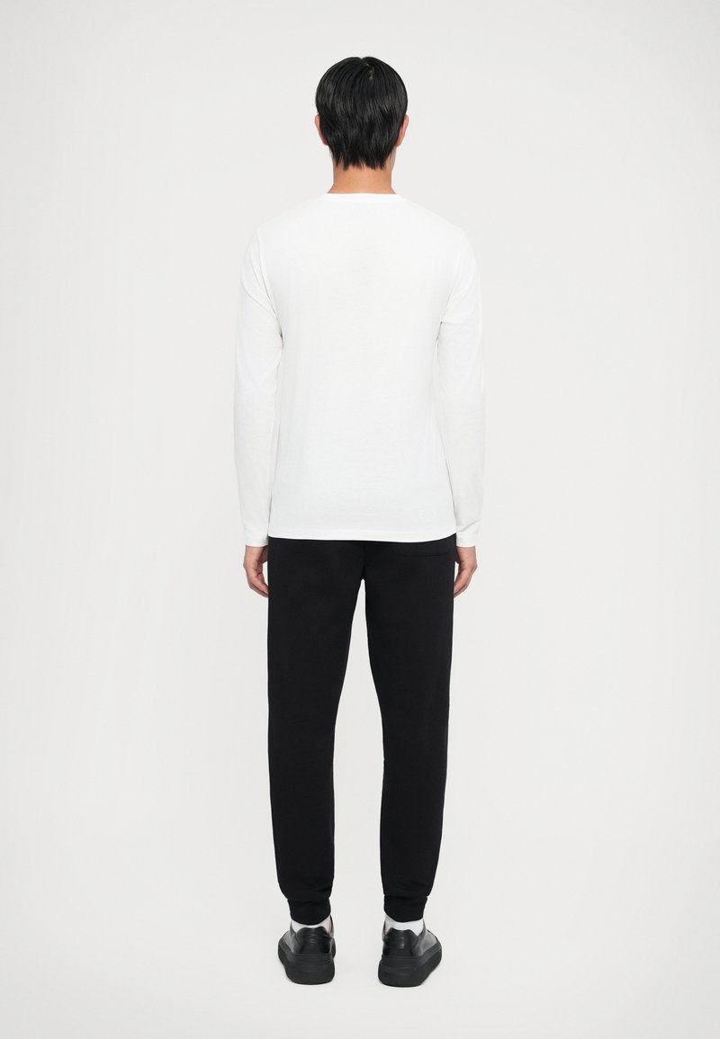 Camisa blanca de manga larga combinada con pantalones de chándal negros. Diseño simple y ajustado, textura suave y acentos minimalistas.