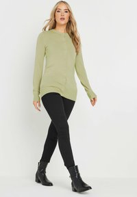 Ljusgrön knappad cardigan med långa ärmar, ribbad textur och rak skärning, matchad med svarta smala jeans och klackade ankelstövlar.