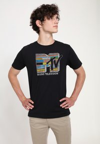 Black t-shirt featuring a multi-colored MTV logo with “MUSIC TELEVISION” text below. Short sleeves, standard fit, smooth fabric texture.