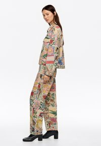 Conjunto de chaqueta y pantalones de patrón floral en beige, con diseños multicolores. Tela suave, corte relajado, complementado con botas negras de tacón grueso.