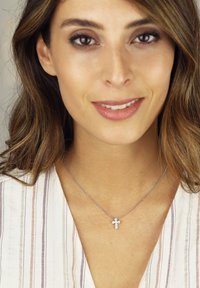 Silberne Kettenhalskette mit einem Kreuzanhänger und klaren Edelsteindetails, vor einem Hintergrund aus leicht gestreiftem Stoff.