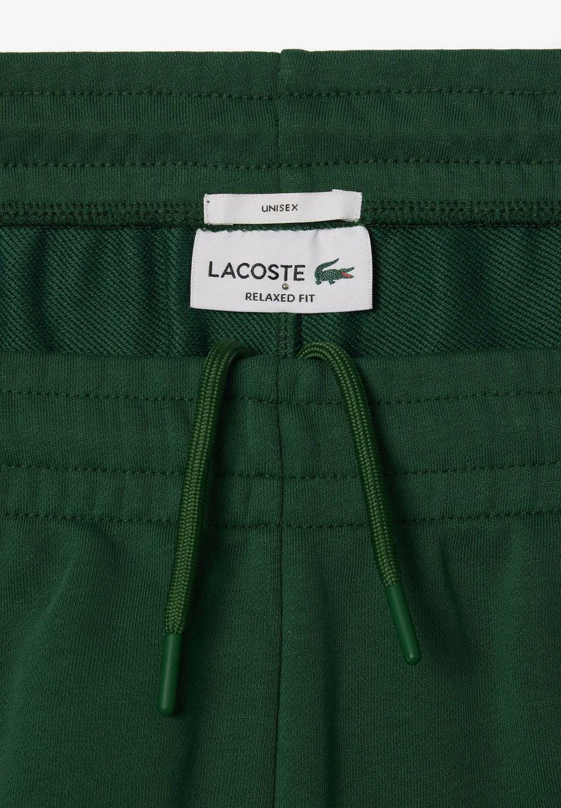 Zielone szorty w luźnym kroju z elastycznym paskiem na sznurku. Posiadają metkę z napisem "LACOSTE" oraz "UNISEX". Wykonane z miękkiego materiału, mają minimalistyczny design.