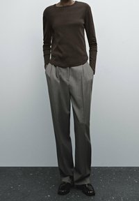 Brown long-sleeve shirt paired with tailored gray pleated trousers and black loafers, set against a plain light background.