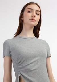 Szary prążkowany t-shirt z krótkim rękawem i okrągłym dekoltem, z delikatnym marszczeniem po bokach. Materiał wydaje się miękki, z dopasowanym krojem i lekką teksturą.