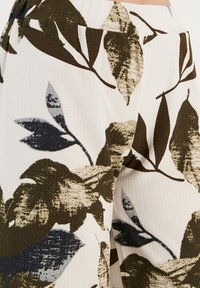 Bloemgepatenteerde stof met grote olijfgroene en marineblauwe bladeren op een lichtromige achtergrond, voorzien van een textuurafwerking en een elastische tailleband.