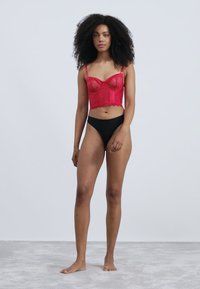 Bralette rossa in pizzo con coppe strutturate e spalline regolabili, abbinata a slip neri a vita alta. Texture liscia, design aderente.