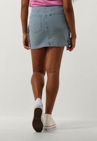 Denim mini-rok in lichtblauw, met twee achterzakken en zijsplitten. Gecombineerd met witte sneakers, wat een casual look laat zien.