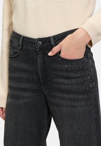 Czarne dżinsy o prostym kroju, z subtelnymi zdobieniami małymi cyrkoniami w pobliżu kieszeni dla dodatkowego detalu.