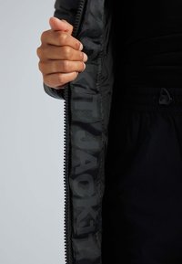 Giacca nera con apertura con zip, che mostra l'interno caratterizzato da un audace testo tonale "JACK1T". Materiale morbido e leggero.