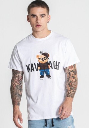 Camiseta de algodón blanca con un gráfico de un oso que lleva gafas, una gorra y ropa. Texto "KAVAGH" impreso debajo del diseño. Corte casual.