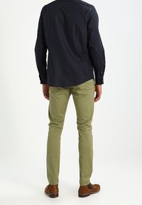 Dark blue long-sleeve shirt with a subtle pattern, paired with olive green slim-fit pants and brown ankle boots.
