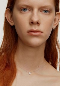 Collar de plata con un colgante circular que presenta una piedra transparente y brillante, lucido sobre piel desnuda debajo de la clavícula. Textura suave.