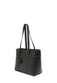Czarna skórzana torba tote z podwójnymi ramiączkami na ramię i przywieszką w kształcie kwiatu przymocowaną do jednego z ramiączek.