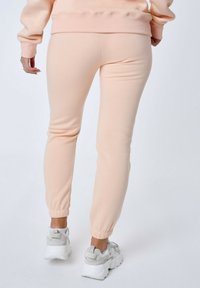 Perzikkleurige sweatpants met een slim fit, elastische boorden en een zachte textuur, gecombineerd met grijze, chunky sneakers.