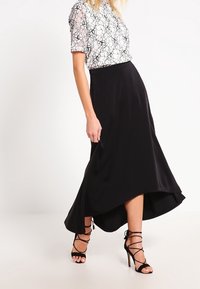 Falda negra de corte asimétrico con una textura suave, combinada con una blusa blanca con un patrón floral negro y mangas cortas. Lleva unos tacones negros con tiras.