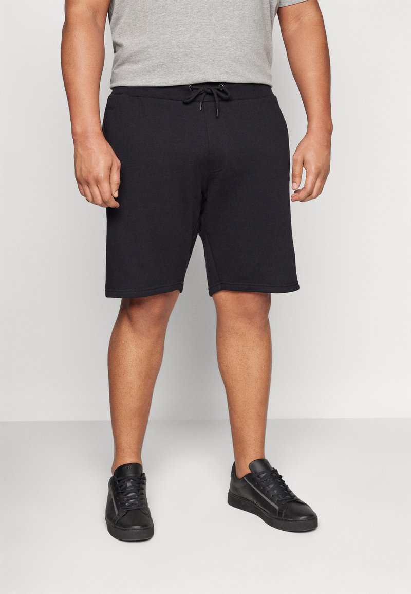 Zwarte katoen shorts met een elastische tailleband en trekkoord. Heeft zijzakken en een knielange snit, gecombineerd met zwarte sneakers.