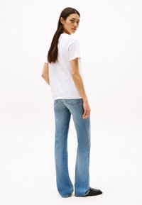 Weißes Baumwoll-T-Shirt kombiniert mit hellblauen Schlagjeans. Das T-Shirt hat kurze Ärmel und einen lässigen Schnitt. Die Jeans haben eine leicht ausgewaschene Textur.