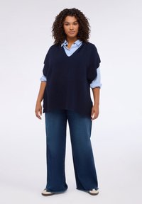 Granatowy dziergany ponczo z szerokim dekoltem i krótkimi rękawami, noszony na jasnoniebieskiej koszuli na guziki. Połączony z szerokimi dżinsami i trampkami.