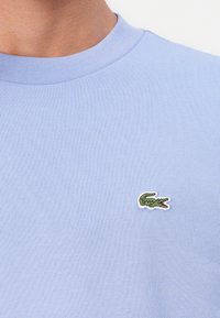 Lyseblå crewneck t-shirt lavet af bomuld, med et lille broderet grønt krokodillelogo på venstre bryst.