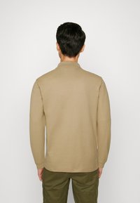 Beiges Poloshirt mit langen Ärmeln, Kragen, weicher Textur und lässiger Passform, kombiniert mit olivgrünen Cargohosen.