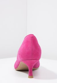 Chaussure à talon haut en daim rose avec un talon fin, présentant une texture lisse et un design à bout arrondi. Aucun logo ou ornement visible.