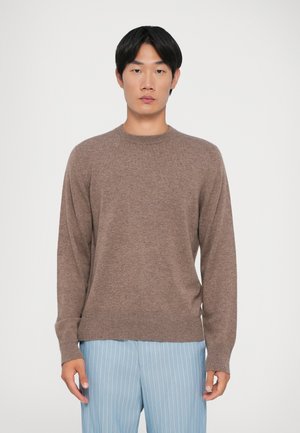 Hnědý pletený svetr s kulatým výstřihem a ribbovanými manžetami; kombinovaný se světle modrými pruhovanými kalhotami. Měkká textura, minimalistický design.