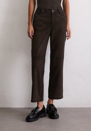 Bruine suède broeken met een rechte pasvorm, voorzien van een knoopsluiting en voorzakken. Gecombineerd met zwarte loafers voor contrast.
