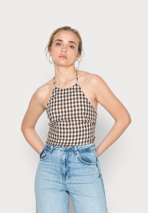 Top halter xadrez marrom e creme com um design ajustado, combinado com jeans de lavagem clara de cintura alta. Superfície de tecido suave.