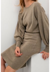 Abito in maglia marrone chiaro, caratterizzato da un collo rotondo, maniche a palloncino e una silhouette aderente con una texture liscia.