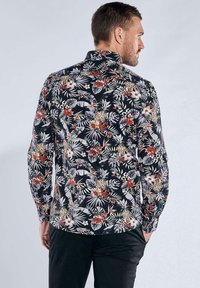 Schwarzes Blumenshirt mit weißen und orangefarbenen tropischen Mustern. Lange Ärmel, Standardkragen und abgerundeter Saum.