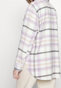 Licht geruit overhemd in lavendel, wit en beige tinten. Zacht stof, afgeronde onderkant, knoopdetails op de manchetten en contrasterende zwarte lijnen.