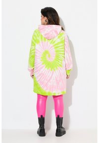 Vestido con capucha de tie-dye en espirales rosa y verde, con mangas largas y un corte en A, combinado con leggins rosas brillantes y botas negras.