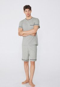 Pijamas de algodón gris de manga corta con ribete negro, que presentan un cuello redondo y un bolsillo en el pecho. Los pantalones cortos tienen un dobladillo con puño.