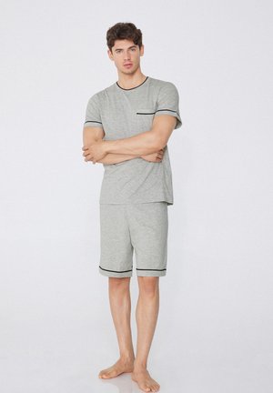 Pijamas de algodón gris de manga corta con ribete negro, que presentan un cuello redondo y un bolsillo en el pecho. Los pantalones cortos tienen un dobladillo con puño.