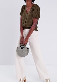 Haut boutonné vert olive avec manches bouffantes, pantalon large crème, chaussures à talons métalliques, et sac rond à motifs noirs et blancs.