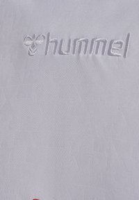 Tessuto bianco con una texture liscia, caratterizzato dal logo "hummel" in rilievo e un accento rosso nella parte inferiore. Design semplice, senza motivi aggiuntivi.