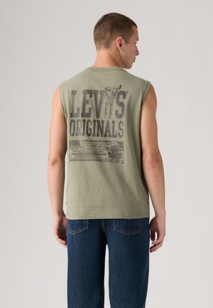 Homme de dos portant un débardeur vert olive avec un grand texte "LEVI'S ORIGINALS" et un graphisme, associé à un jean bleu.