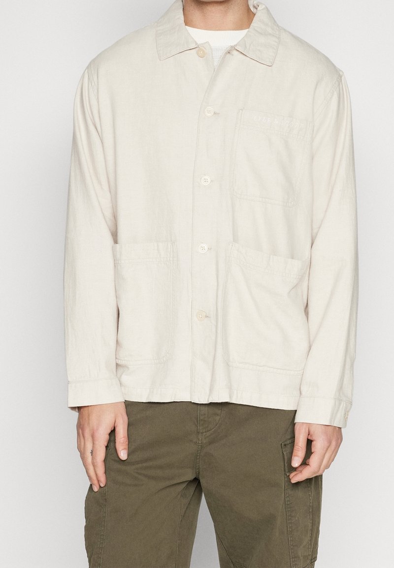 Beige, langslippige knoopshirt gemaakt van lichtgewicht stof, met een puntige kraag, twee voorzakken en subtiele stikdetails.