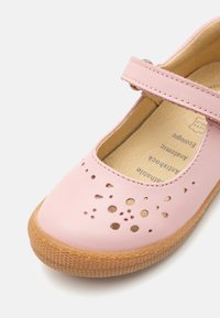 Zapato Mary Jane de cuero rosa con diseño perforado en la puntera, suela de goma beige y correa ajustable. Forro de cuero natural visible en el interior.