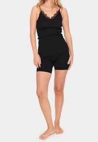 Svart linne med spetsdetaljer och scalloped fåll, kombinerat med svarta cykelbyxor. Båda plaggen är ribbade och följsamma.