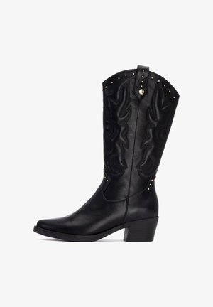 Botas de vaquero de cuero negro con costuras decorativas, punta afilada, tacón de bloque de altura media y tachuelas metálicas a lo largo del borde superior.