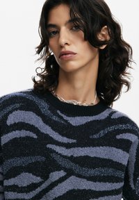 Maglione lavorato a maglia con un motivo a strisce zebra nero e grigio, con un colletto nero a costine e una finitura in tessuto morbido e texturizzato.
