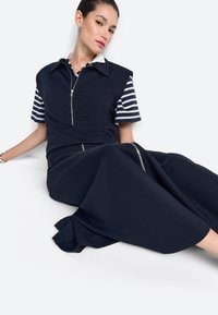 Tengerészkék cipzáras ruha rövid csíkos ujjakkal, gallérral és enyhén bővülő alsó résszel. Simogató tapintású anyag és minimális fém díszítés.