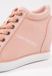 Růžové plátěné kotníkové tenisky s kulatou špičkou, šněrováním na přední straně a bílou gumovou podrážkou. Logo 'Calvin Klein Jeans' je zobrazeno v bílé barvě.