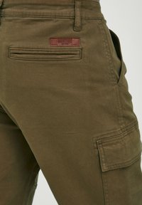 Pantalons cargo vert olive en coton lisse, dotés d'une poche latérale, d'une poche arrière avec couture et d'un petit logo en cuir marron.
