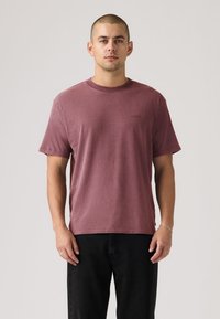 Μπορντό βαμβακερό T-shirt με στρογγυλή λαιμόκοψη. Κοντά μανίκια και άνετη εφαρμογή. Διακριτική λεπτομέρεια με λογότυπο στο στήθος, σε συνδυασμό με σκούρο τζιν.