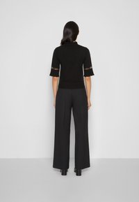 Top negro de manga corta con dobladillo ondulado y detalles de encaje, combinado con pantalones negros de pierna ancha de cintura alta y botas con tacón grueso.