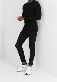 Pull noir côtelé, jean noir moulant avec genou déchiré, et chaussures de sport blanches. Tenue décontractée au design épuré et aux couleurs contrastées.
